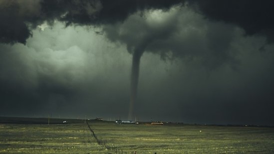 Tornado funnel cloud forming over open farmland under dark stormy skies in the Upper Midwest.
