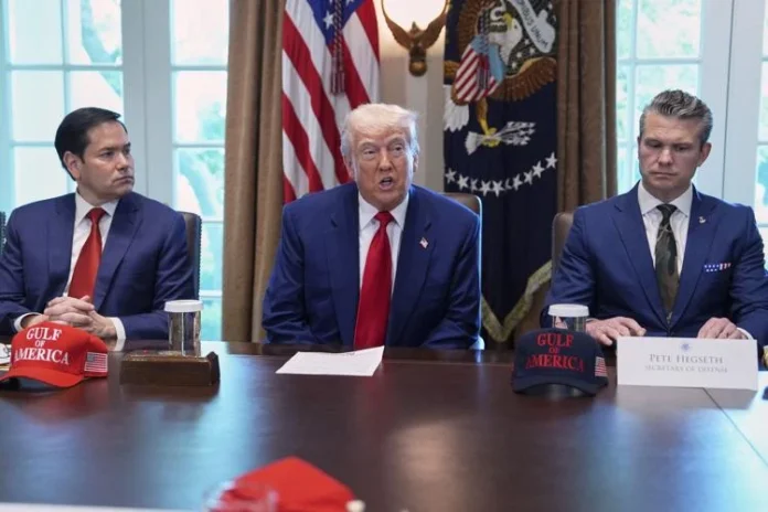 Donald Trump speaks at a table flanked by Marco Rubio and Pete Hegseth, with U.S. flags and the presidential seal in the background during a national security briefing.
