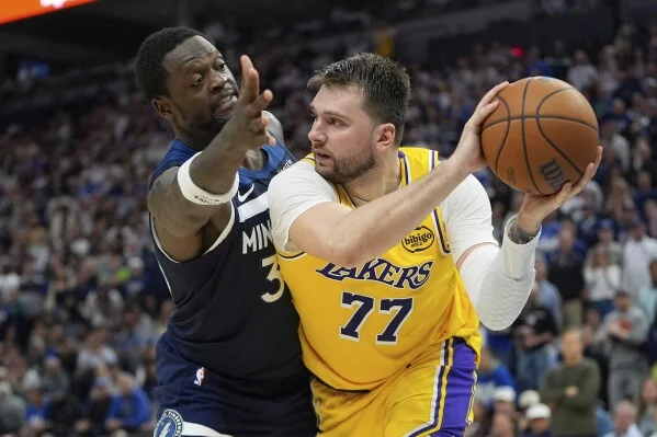 Luka Dončić in a yellow Lakers jersey holds the ball under pressure from a Minnesota Timberwolves defender during Game 5 of the NBA Playoffs.