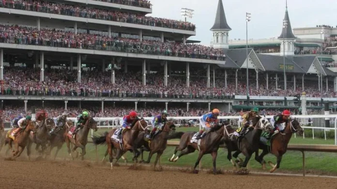 Thoroughbred horses race down the track at Churchill Downs during the Kentucky Derby with a packed grandstand in the background.