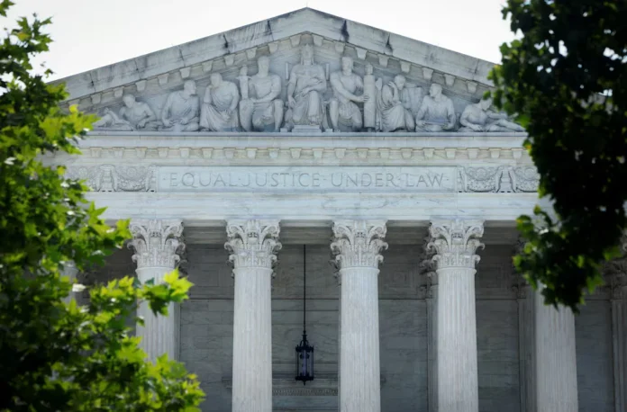 Front view of the U.S. Supreme Court with “Equal Justice Under Law” inscribed above its columns, framed by tree branches.